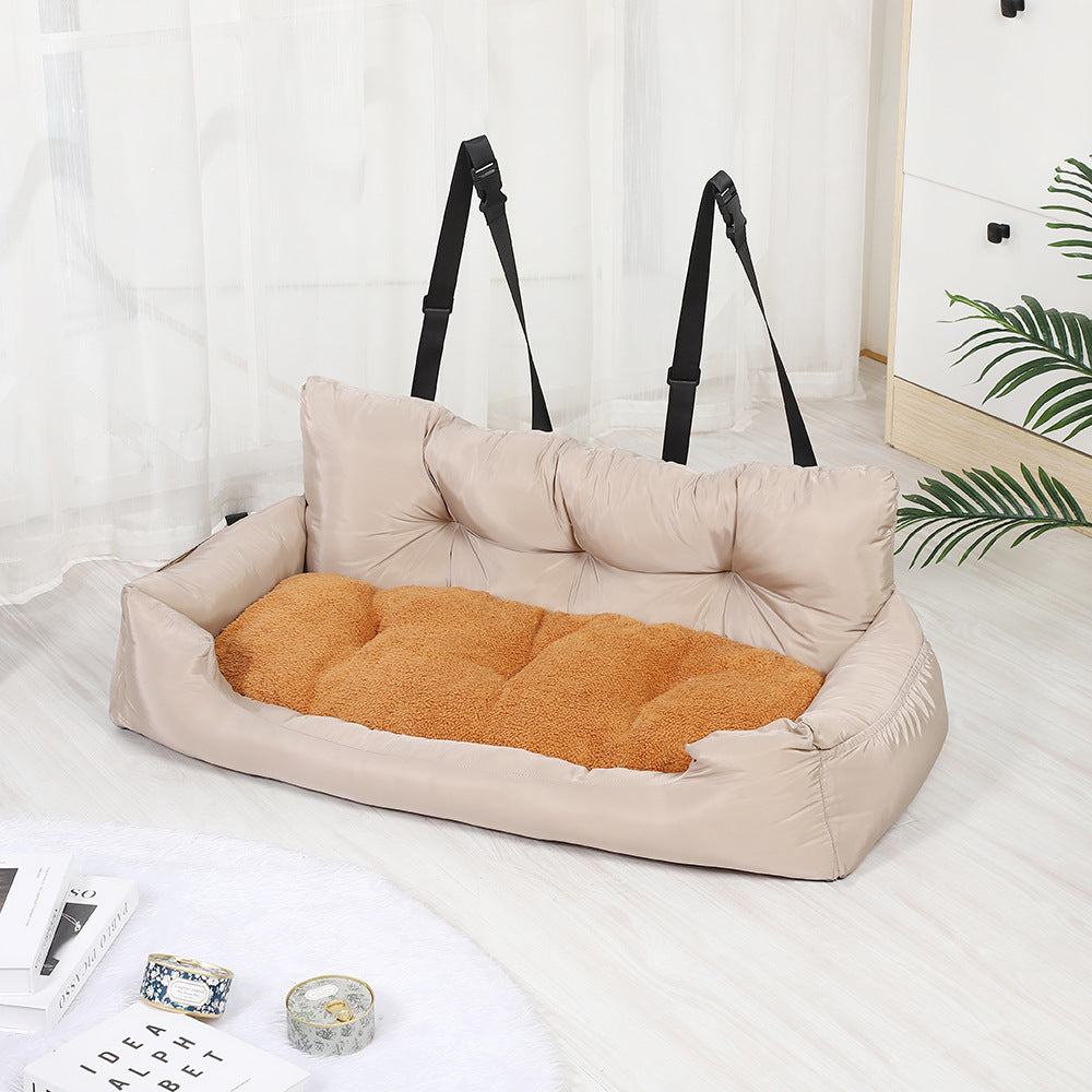 Beige pet bed with orange cushion on a white surface, with black straps in the background.